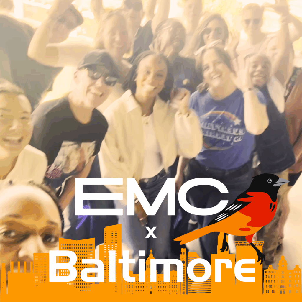 Team group photo with city skyline across the bottom. Text reads EMC x Baltimore. Raven bird.